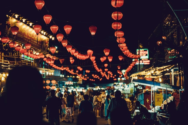 people walking between food stalls under chinese lanterns