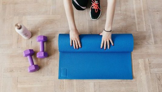 Practical Tips for Organizing a Highly Effective Home Gym Home Gym - Top view of anonymous female athlete in black leggings and sneakers unfolding blue mat for exercising on floor near dumbbells and water bottle in modern fitness center